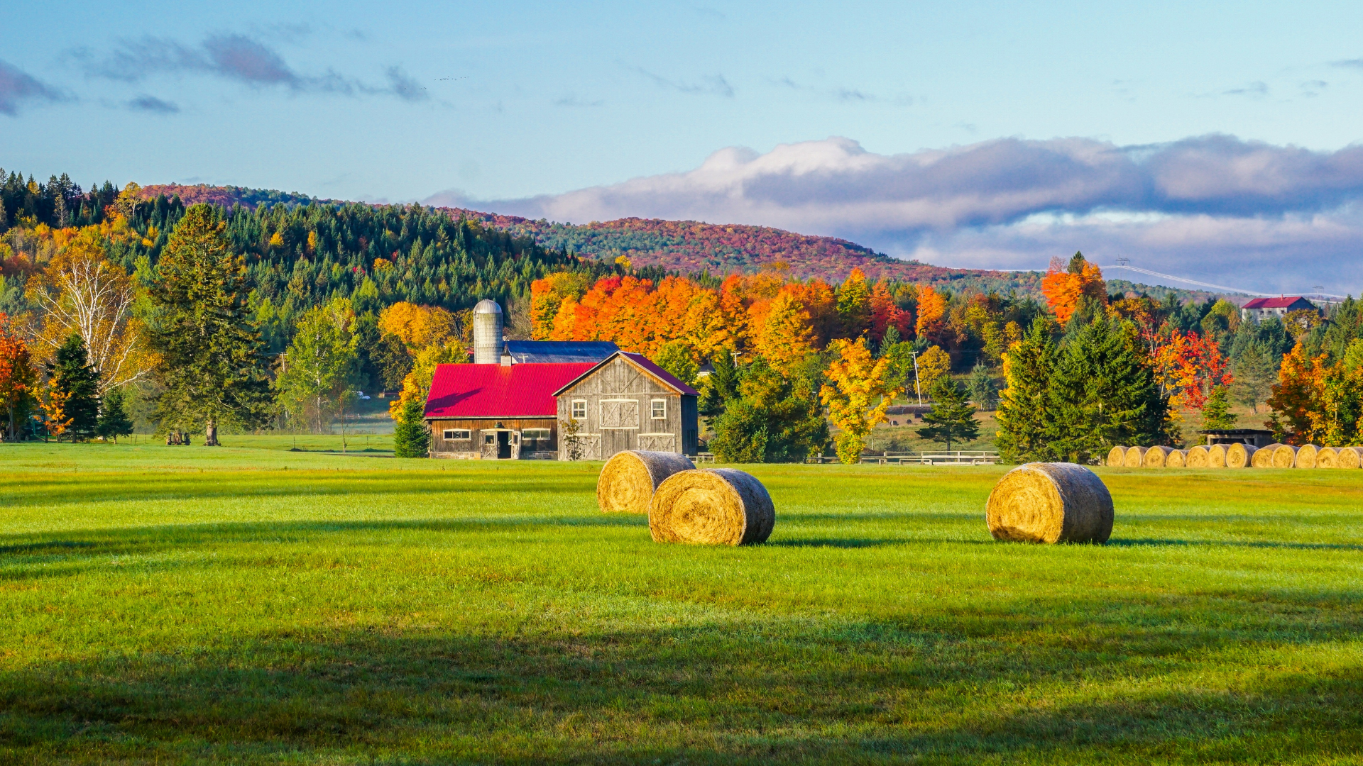 Farm buildings, hay bales, and fields surrounded by colorful autumn trees